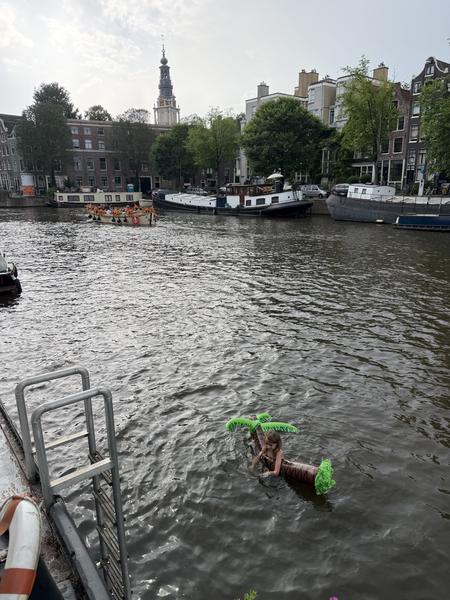 A person floats playfully in the water with an inflatable palm tree on the Oudeschans canal in Uilenburg, Amsterdam
